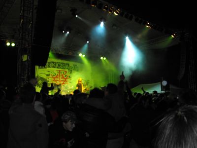 Zöld és fehér fényekkel megvilágított szabadtéri koncert közönséggel.